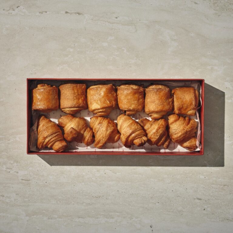 קופסה מלבנית של "בוקר צרפתי" עם חמישה מאפים מרובעים וחמישה מאפים בצורת קרואסון מסודרים בשתי שורות על משטח בהיר. - Cassarole