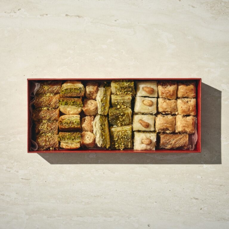 קופסה מלבנית של בקלאוות, מלאה במאפים מזרח תיכוניים שונים המסודרים בשורות מסודרות על משטח בהיר. - Cassarole