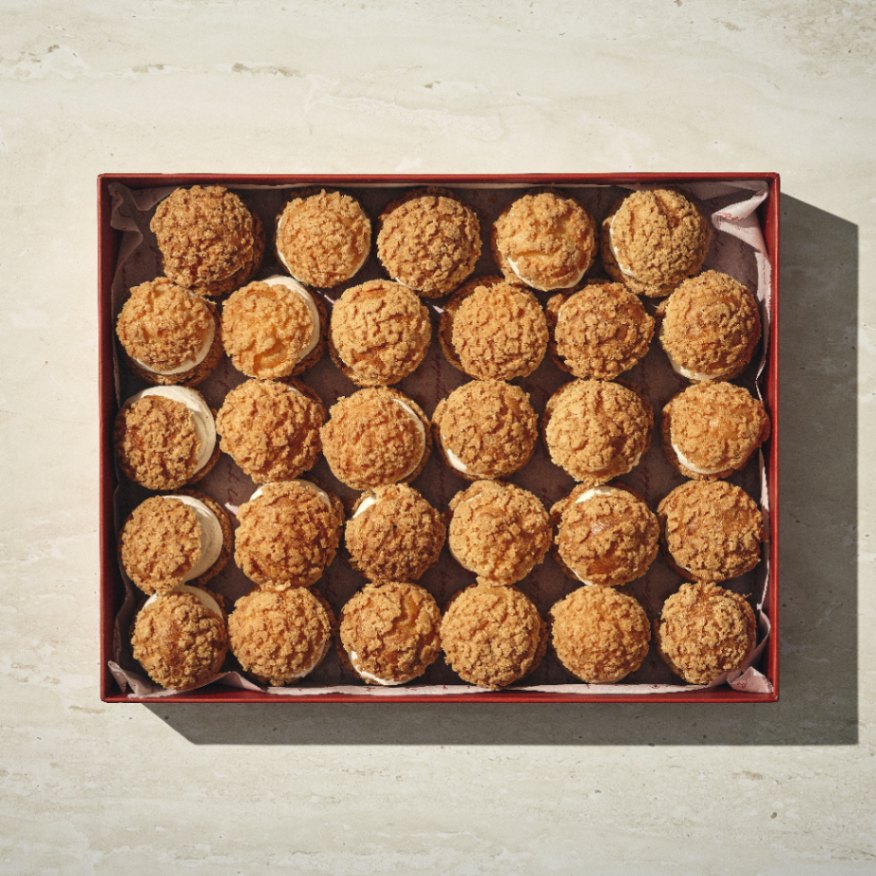 קופסה של 25 "הפחזניות של קסרולה" מאפים ממולאים בקרם, מסודרים ברשת 5x5 על משטח בהיר. - Cassarole