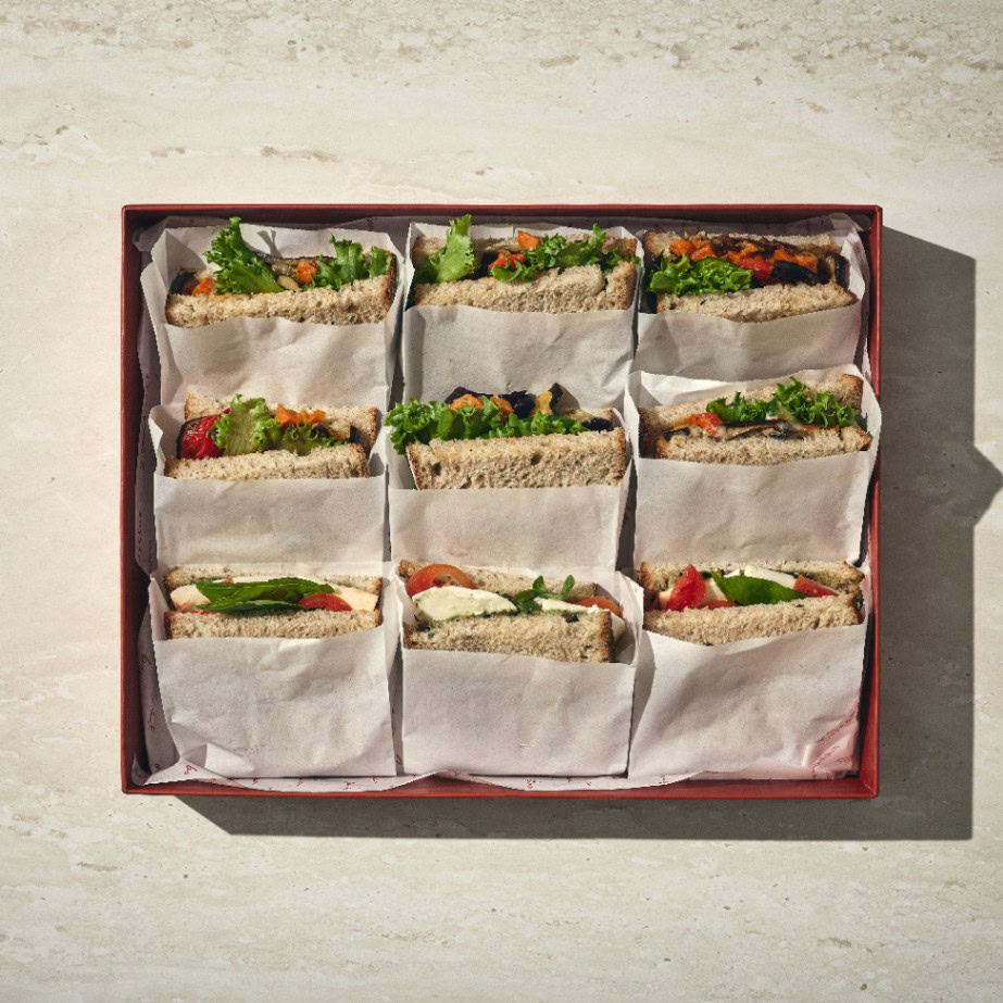 מבט מלמעלה על קופסה המכילה תשעה כריכים מחמצת, כל אחד עטוף בנייר אפייה, מסודרים בקפידה על משטח בצבע בז'. - Cassarole