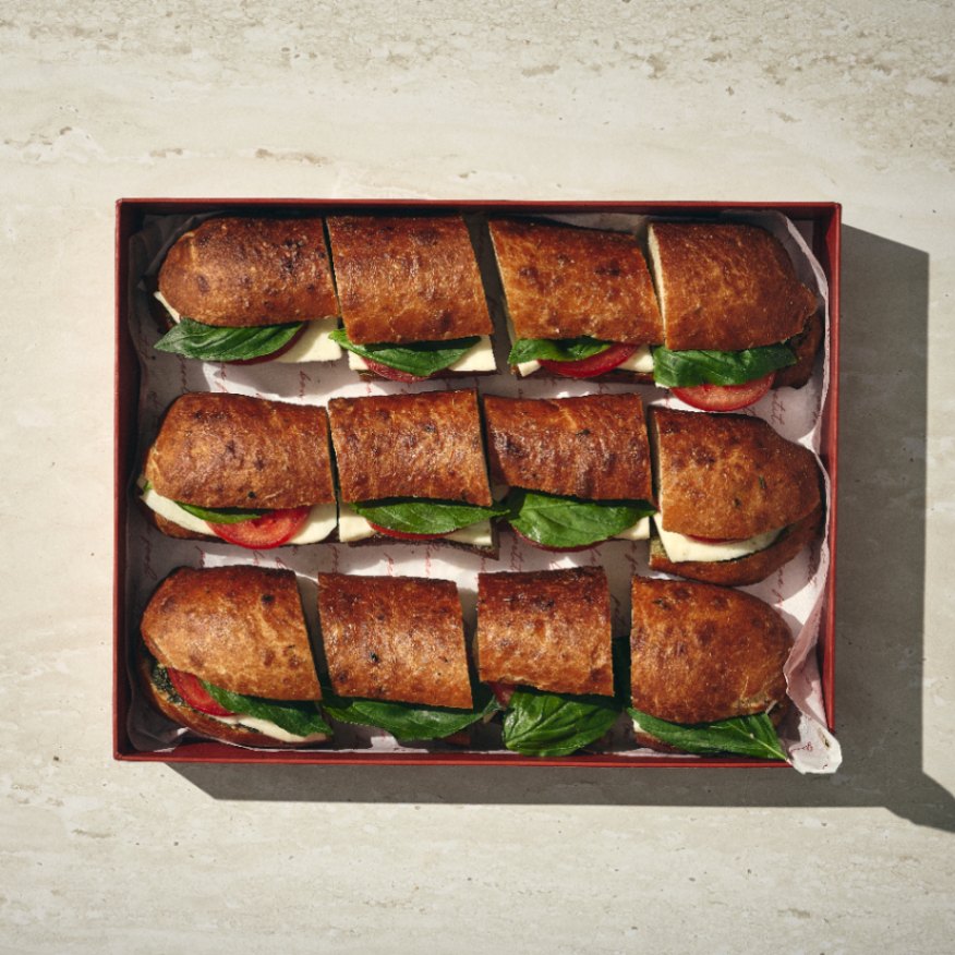 שני כריכי פוקאצ'ות ממולאים בעגבנייה, מוצרלה ובזיליקום, כל אחד חתוך לשש חתיכות ומסודר בקפידה בקופסה מלבנית על משטח בהיר. - Cassarole