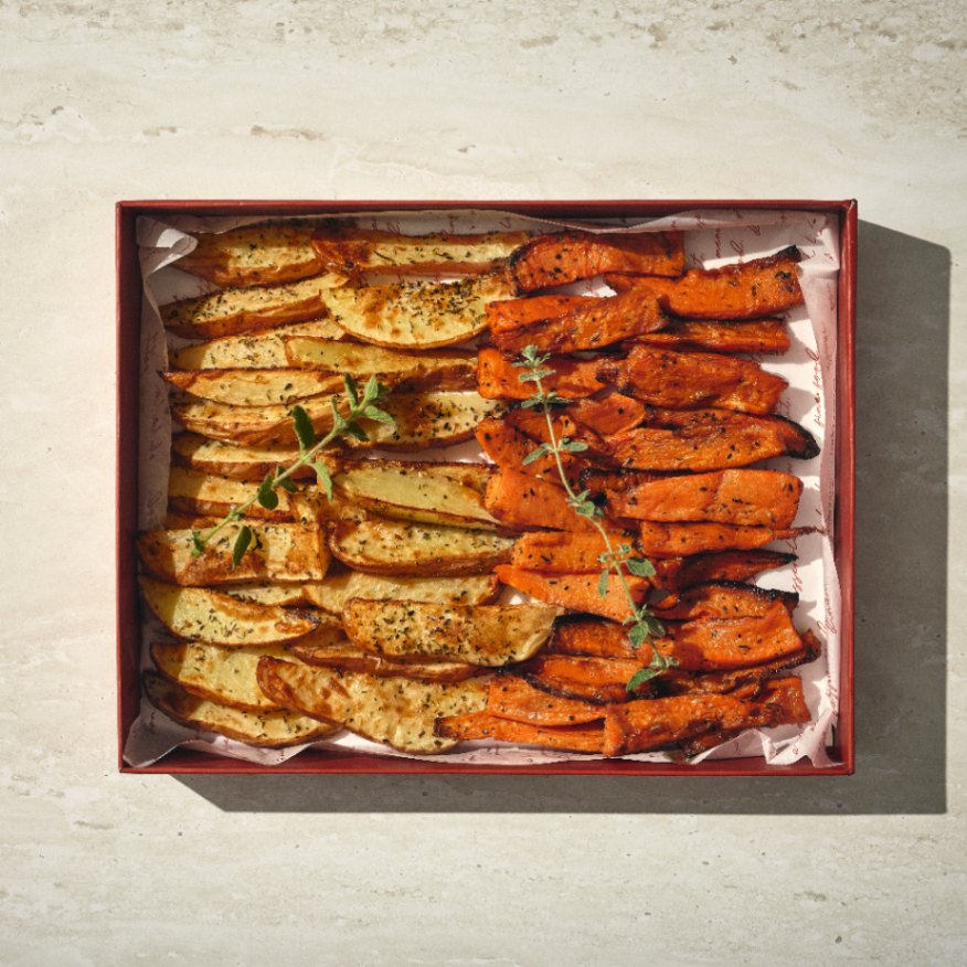 קופסה של מיני תפוחי אדמה ובטטה עם פלחי תפוחי אדמה מתובלים משמאל ומקלות בטטה קלויים מימין, מעוטרים בעשבי תיבול טריים. - Cassarole