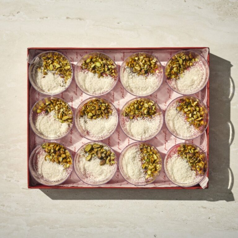 קופסה של 12 קינוחי מלבי, כל אחד מהם עגול ומצופה בפיסטוקים קצוצים וקוקוס מגורר, מסודרים בשלושה טורים על משטח בהיר. - Cassarole