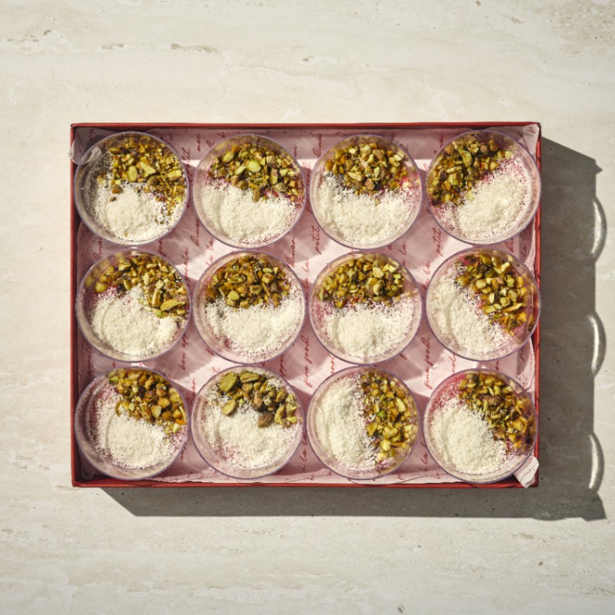 קופסה של 12 קינוחי מלבי, כל אחד מהם עגול ומצופה בפיסטוקים קצוצים וקוקוס מגורר, מסודרים בשלושה טורים על משטח בהיר. - Cassarole