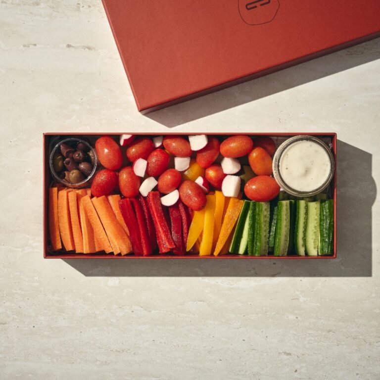 קופסה מלבנית של נשנושי בריאות (קטן) עם עגבניות שרי, חתיכות מוצרלה, גזר, פלפל אדום וצהוב, מקלות מלפפון, זיתים שחורים וכוס רוטב ראנץ'. - Cassarole