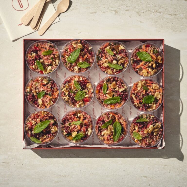 12 מנות של סלט קינואה אישי בכוסות שקופות, כל אחת מעוטר בעלי נענע, מסודרות בקפידה על מגש עם כפות עץ ומפית על משטח אבן בהיר. - Cassarole