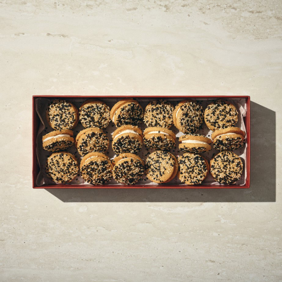 קופסה מלבנית של עוגיות פרמזן מכילה שלוש שורות של עוגיות עגולות מצופות בשומשום שחור, מסודרות בקפידה על משטח בהיר. - Cassarole