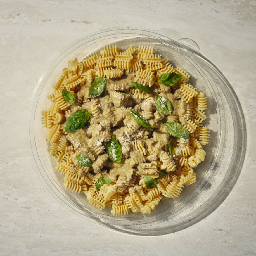 פסטה מסולסלת בקופסה עגולה מפלסטיק, עם רוטב שמנת, עלי בזיליקום טריים וגבינה מגוררת, מונחת על משטח בהיר. - Cassarole