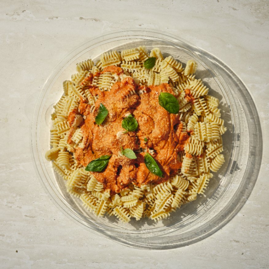 קערה שקופה של פסטה מסולסלת עם רוטב אדום שמנת ועלי בזיליקום טריים, מוגשת על משטח בהיר. - Cassarole