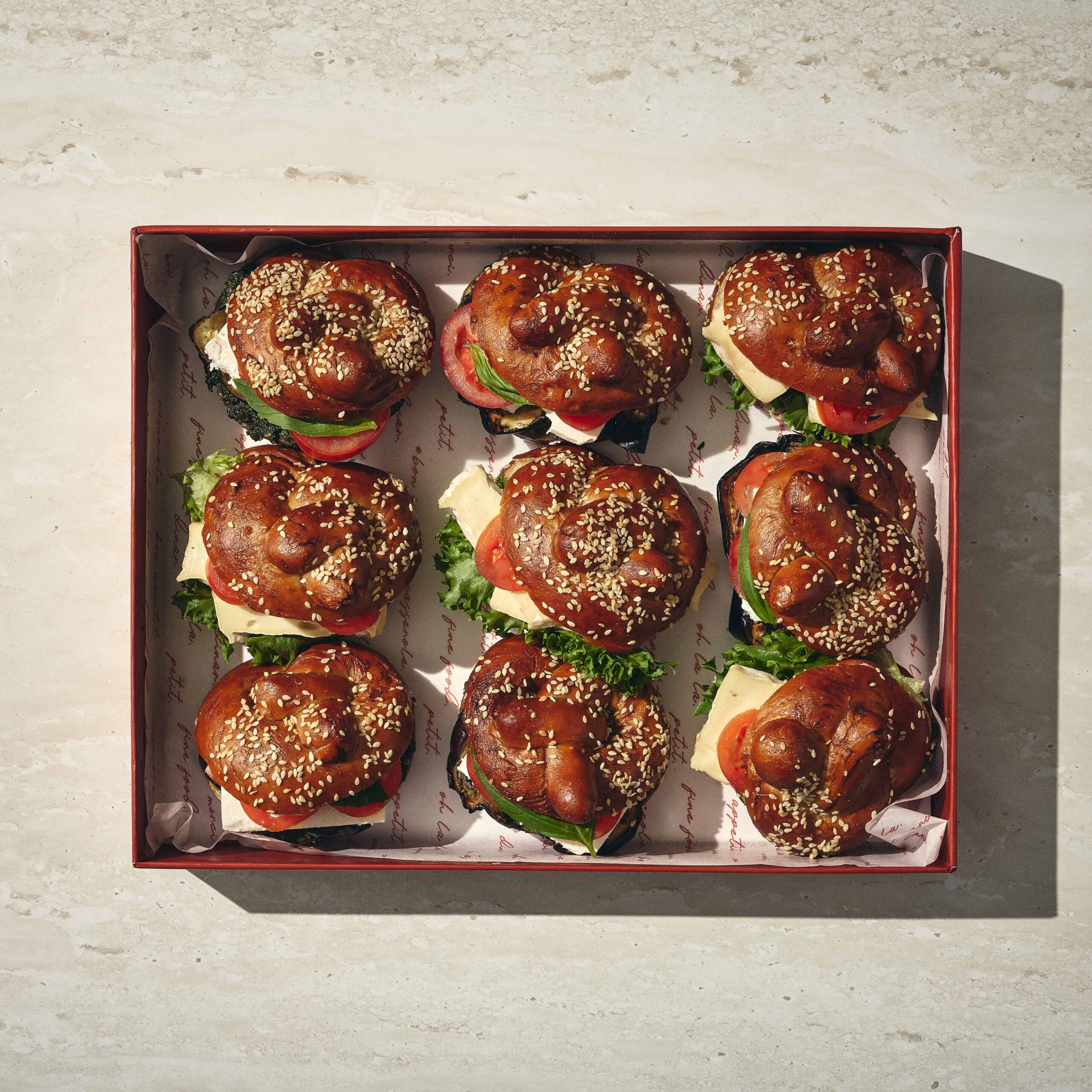 קופסה המכילה תשעה כריכי לחמניות פרצל עם חסה, עגבנייה וגבינה, מסודרים ברשת 3x3 על נייר אפייה. - Cassarole