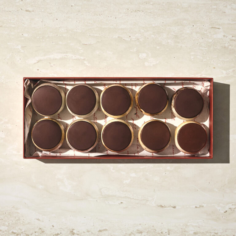 קופסה מלבנית המכילה עשרה קינוחים עגולים עם ציפוי שוקולד מריר, מסודרים בשתי שורות של חמישה, על נייר אפייה בהיר. - Cassarole