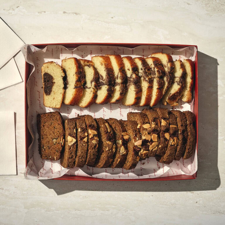 קופסה עם שתי שורות של עוגות פרוסות: אחת בהירה עם מערבולת כהה, והשנייה כהה עם אגוזים מעל. שתי מפיות מקופלות מונחות לצד הקופסה. - Cassarole