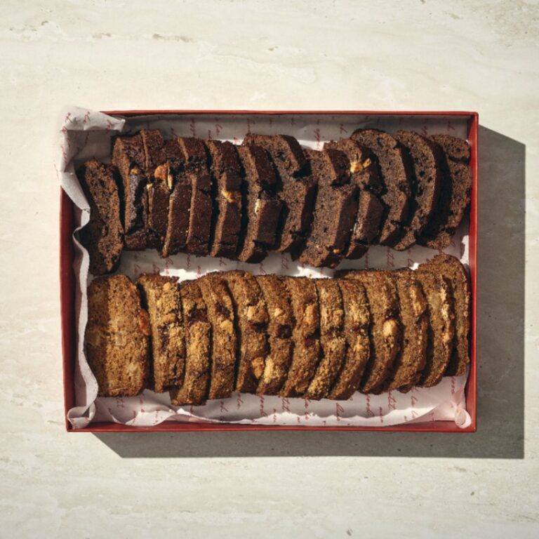 קופסה מלבנית עם הכיתוב "מארז זוגי עוגות שוקולד ותפוחים" מכילה שתי שורות של פרוסות עוגה מסודרות בקפידה, אחת שוקולד (כהה יותר) ואחת תפוחים (בהירה יותר), על נייר לבן. - Cassarole