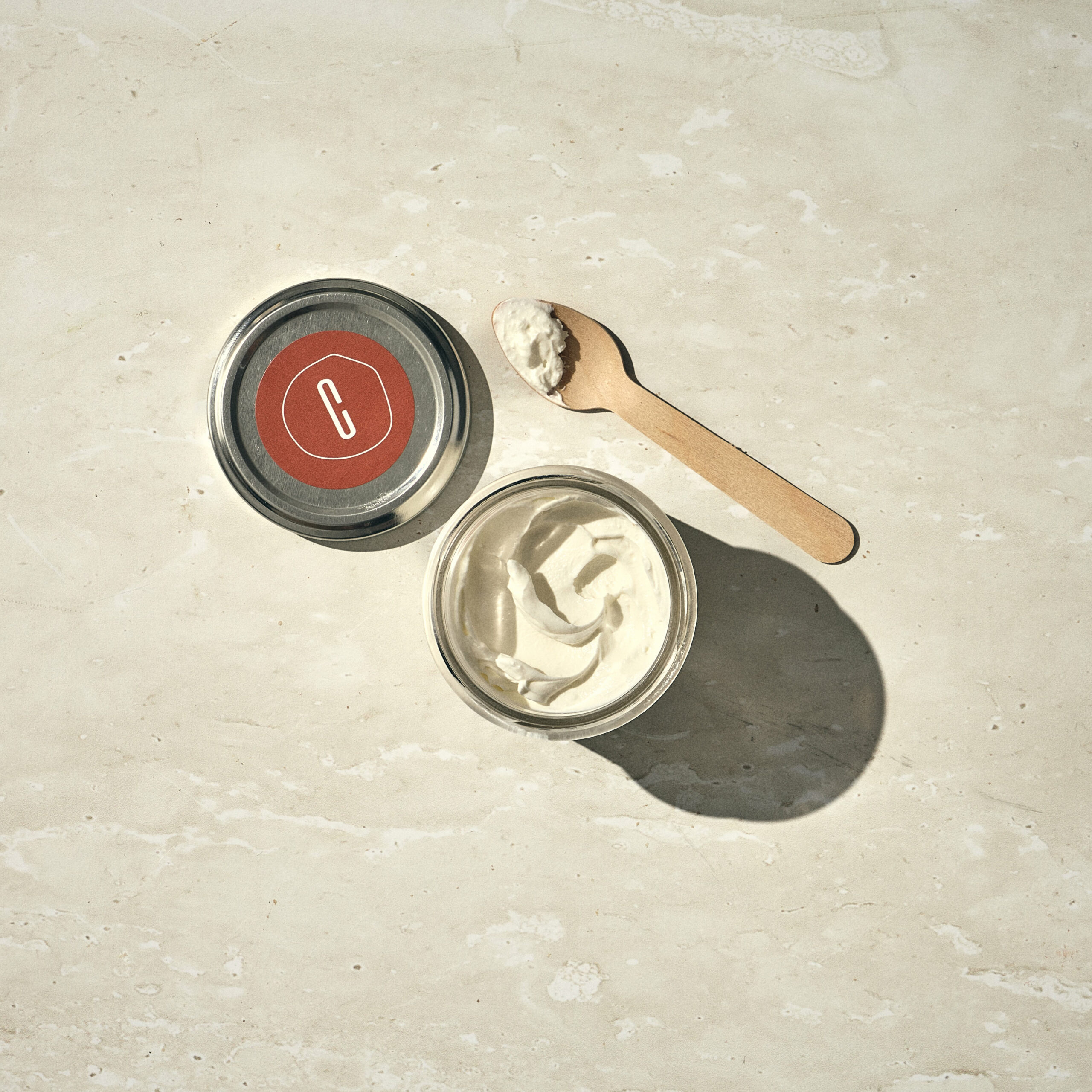 צנצנת זכוכית של שמנת עם מכסה מתכת וכף עץ על משטח אבן בהיר. - Cassarole