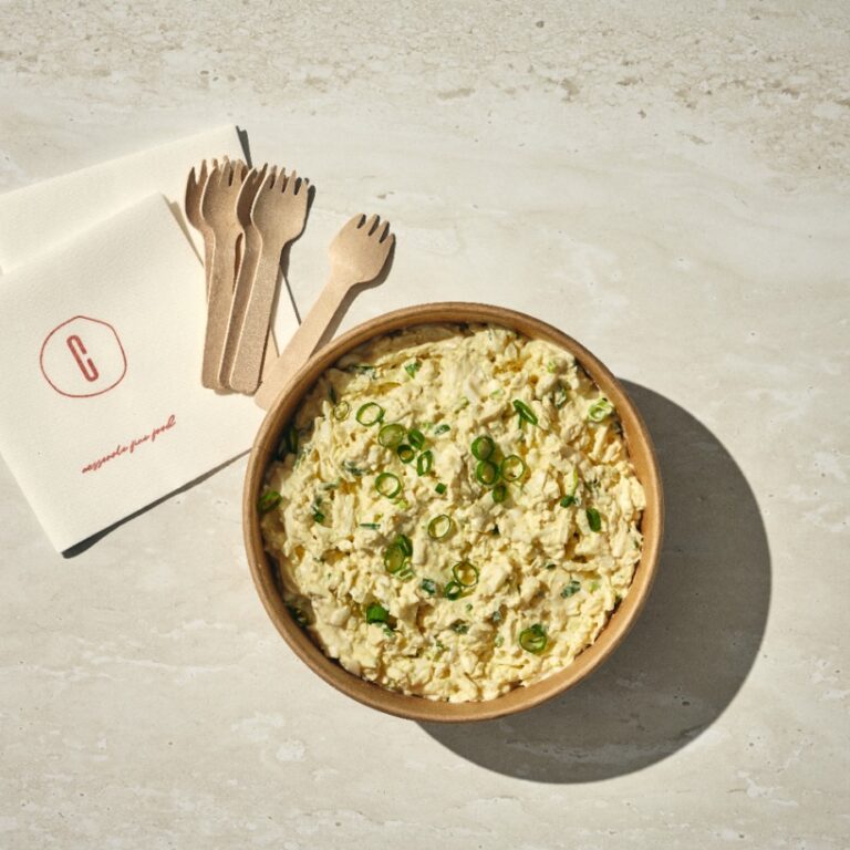 קערת עץ עם סלט ביצים מונחת על משטח בהיר, מקושטת בבצל ירוק קצוץ ומונחת ליד מפיות וארבע מזלגות עץ. - Cassarole