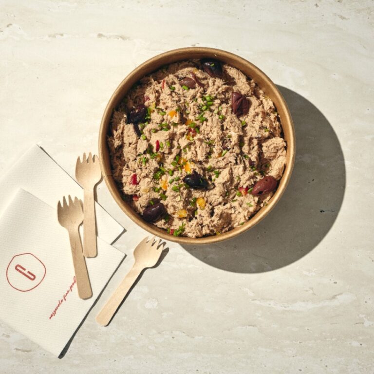 קערת סלט טונה מעוטרת בזיתים ועשבי תיבול מונחת על משטח בהיר לצד שלוש מזלגות עץ ומפית מקופלת. - Cassarole