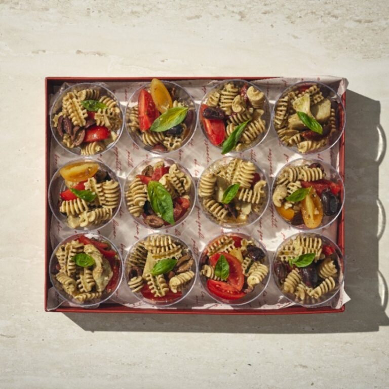 קופסה מכילה 12 כוסות שקופות, כל אחת מהן מלאה בפסטה רוטיני, עגבניות שרי, זיתים ועלי בזיליקום על מצע בהיר. - Cassarole