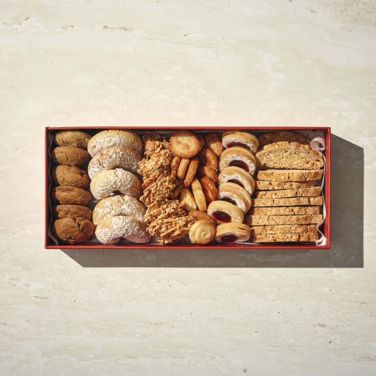 קופסה מלבנית מלאה במבחר עוגיות, כולל ביסקוטי, עוגיות במילוי ריבה, עוגיות אבקת סוכר ועוגיות שיבולת שועל, מסודרות בשורות מסודרות על משטח בהיר. - Cassarole