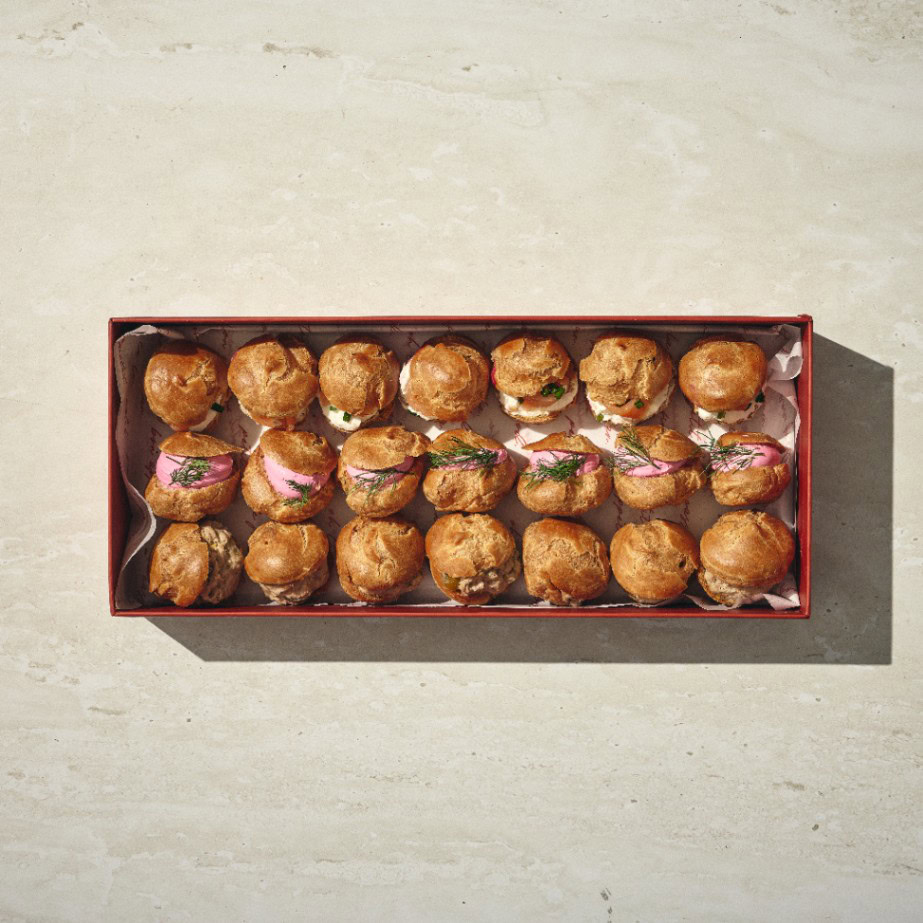 קופסה מלבנית של פחזניות מלוחות — עשרים פחזניות מלוחות, חלקן מעוטרות בעשבי תיבול וקישוטים ורודים, מסודרות בקפידה בארבע שורות על משטח בהיר. - Cassarole